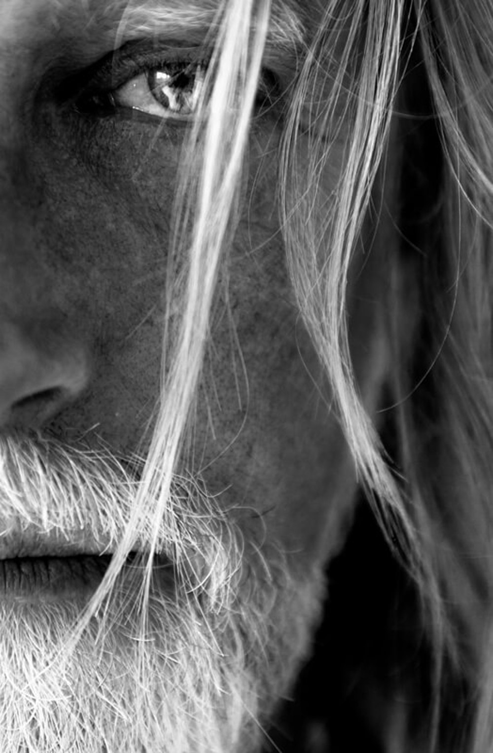 Nahaufnahme des Gesichts eines Mannes mit grauen Haaren und Bart, ein Auge ist sichtbar, Schwarz-Weiß.