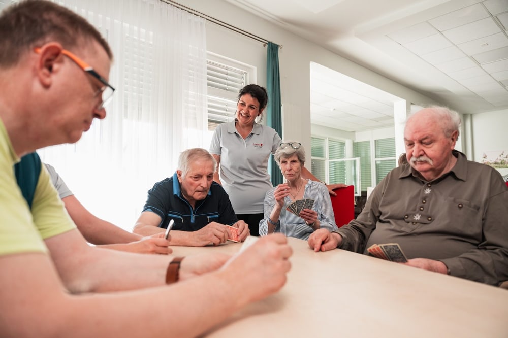 Pflegekraft mit Bewohnern beim Spielen am Tisch