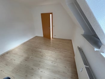 Leeres Zimmer mit Blick zur offenen Tür und Heizkörper unter der Dachschräge