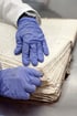 Hände in blauen Handschuhen reinigen die Seiten eines alten, beschädigten Buches mit einem Schwamm.