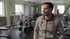 Mann im grauen Hoodie mit grünem Fitz Fitness Logo steht in einem Fitnessstudio voller Trainingsgeräte für eine Imagefilm-Produktion.