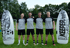 Vier Fußballspieler in grauen Trikots und schwarzen Shorts stehen zwischen zwei aufblasbaren "KEEPERsport"-Trainingspuppen auf dem Rasen.