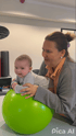 Eine Frau hält ein Baby, das auf einem großen grünen Gymnastikball liegt.