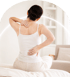 Woman sitting on a bed holding her neck and lower back in pain.