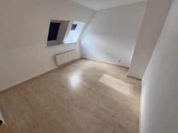 Leeres Dachzimmer mit zwei kleinen Fenstern und schräger Decke