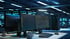 Zwei Computermonitore auf einem Schreibtisch zeigen Code in einem dunklen Serverraum mit blau leuchtenden Lichtern an.