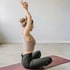 Frau im Yoga-Outfit meditiert auf einer roten Matte mit erhobenen Armen.