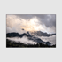 Misty mountains with thick clouds and a bright glimmer of light behind them, dark forests in the foreground.