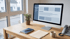 Moderner Arbeitsplatz mit Desktop-Monitor, Website-Layout, Notizbuch, kleiner Pflanze und Kaffeetasse auf einem Holztisch.
