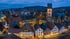 Luftaufnahme einer beleuchteten Altstadt mit Fachwerkhäusern und einer Kirche bei Dämmerung vor bewaldeten Hügeln.