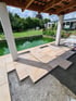Terrasse im Bau mit hellen Natursteinplatten auf Splittbett neben einem Pool im Garten unter einer Holzüberdachung.