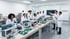 Eine Gruppe von Ingenieuren und Wissenschaftlern in weißen Laborkitteln arbeitet in einem Elektroniklabor.