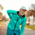 Older man in turquoise jacket and white cap outdoors, holding his back in pain – Chronic Pain Treatment