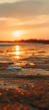 Die untergehende Sonne spiegelt sich auf der feuchten Sandoberfläche eines Strandes bei warmem orangefarbenem Licht.