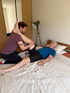 Ein Mann dehnt das Bein eines älteren Mannes, der auf einem Bett liegt.