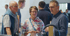 Drei Erwachsene unterhalten sich auf einer Messe, ein Mann in blauem Hemd und eine Frau in Blumenbluse hören einem Mann in Jeanshemd zu.