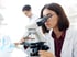 Doctor in a lab coat examines a petri dish under a microscope during lab testing.