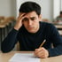 Ein junger Mann sitzt mit besorgtem Blick an einem Schreibtisch und hält einen Bleistift über einen Multiple-Choice-Test.