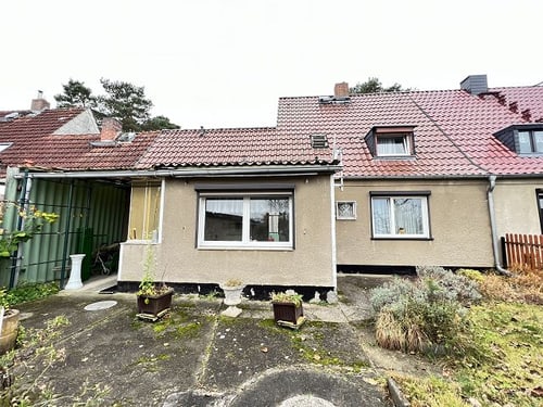 Rückansicht eines Reihenhauses mit kleiner Terrasse, grünem Schuppen, brauner Fassade und roten Ziegeldächern.