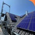 Dunkles Ziegeldach mit installierten blauen Solarmodulen und einem Baugerüst im Vordergrund unter blauem Himmel.