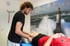 Physiotherapeut behandelt das Knie eines Patienten auf einer Liege vor einer Wand mit Leuchtturm-Motiv.