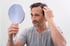 A worried man with thinning hair looking in a mirror.
