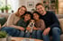 Eine lächelnde Familie mit zwei Kindern und einem kleinen Hund sitzt gemeinsam auf einem Sofa im Wohnzimmer.
