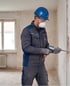 Handwerker mit blauem Helm, Schutzbrille und Atemschutzmaske führt eine Mauersanierung mit einem Injektionsgerät durch.