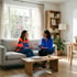 Two women sit on a light gray sofa in a bright living room, talking and gesturing.