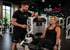 Ein Personal Trainer lächelt eine Frau an, die an einer Beinpresse im "club vital FITNESS & GESUNDHEIT" trainiert.