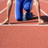 Ein Läufer in blauen Shorts und Schuhen in Startposition auf einer roten Laufbahn.