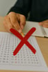 Hand hält einen Stift über einem Multiple-Choice-Testbogen, der mit einem großen roten Kreuz markiert ist.