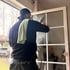 Mann in schwarzer Kleidung mit grünem Tuch reinigt ein weißes Fenster von innen.