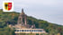 Das Kaiser-Wilhelm-Denkmal an der Porta Westfalica vor bewaldetem Hang mit dem Stadtwappen von Minden oben links.