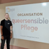 Ein Mann steht vor einer weißen Leinwand mit dem Text "ORGANISATION queersensible Pflege".