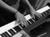 Hände spielen auf den Tasten eines schwarzen Klaviers oder Keyboards.