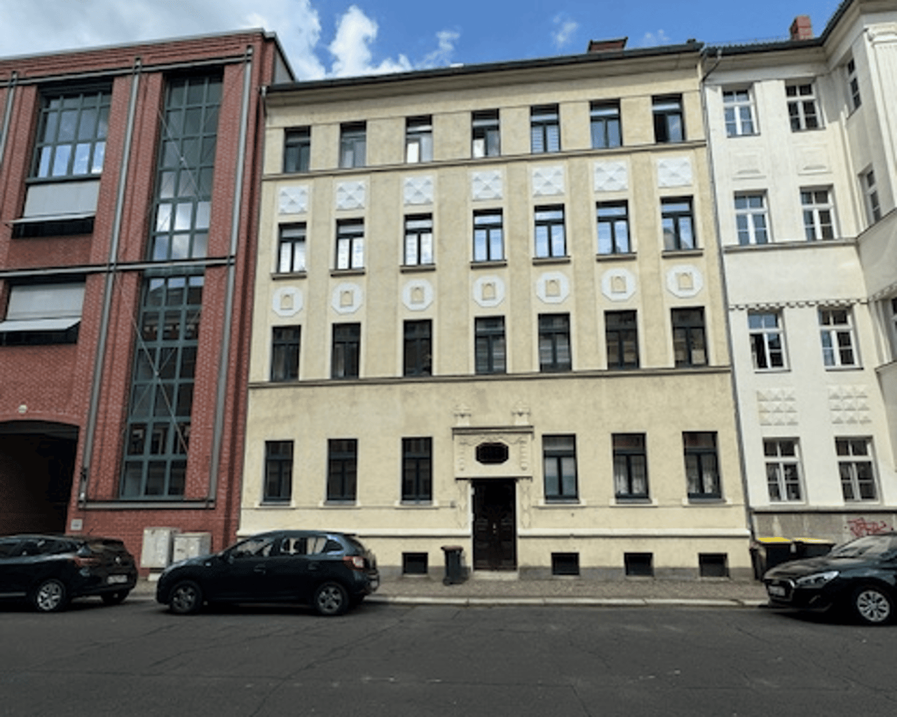 Straßenansicht des Mehrfamilienhauses mit heller Putzfassade und Klinkerteil, davor parkende Autos