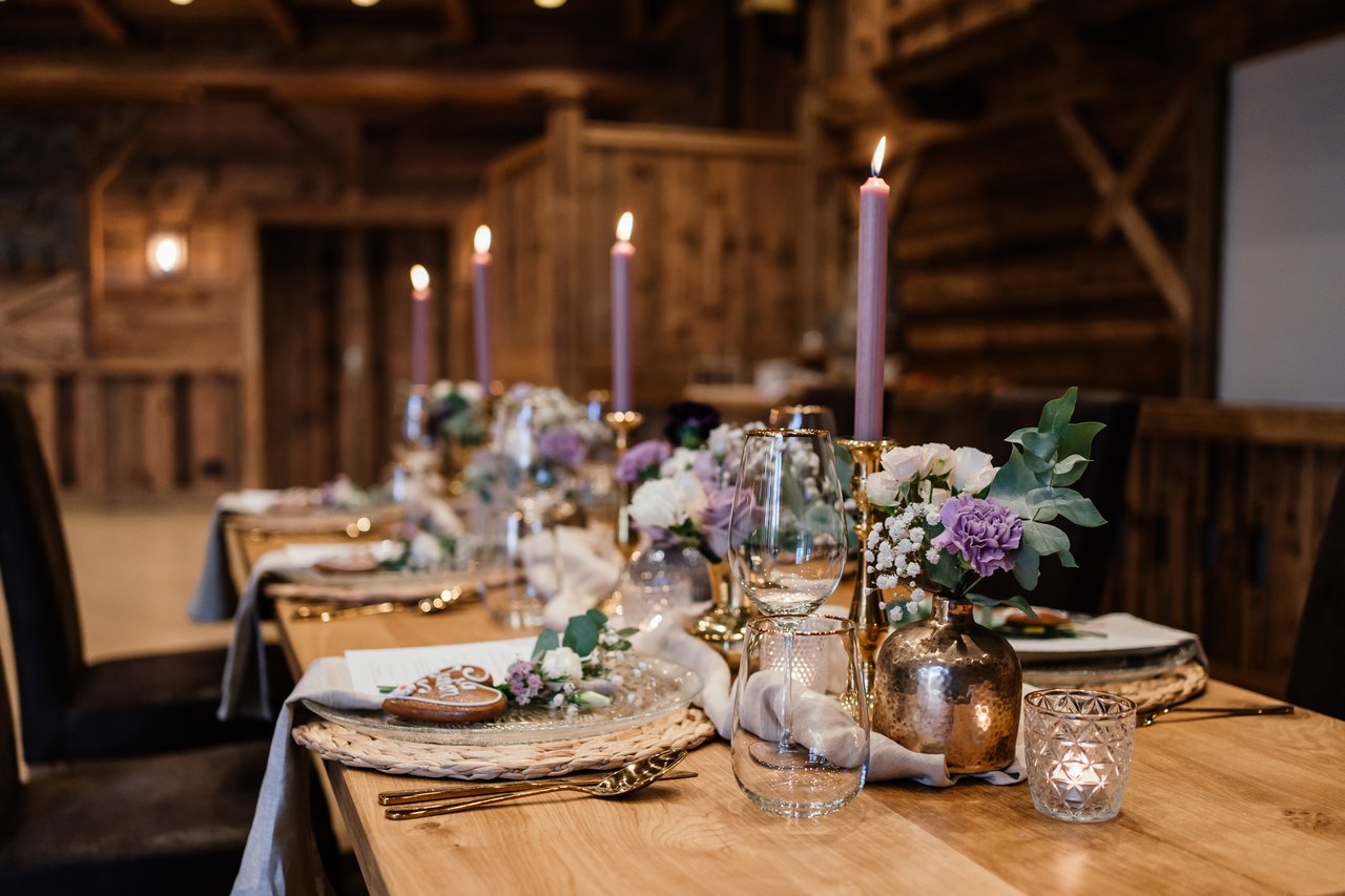 Festlich gedeckte Hochzeitstafel in der Almhütte mit lila Kerzen, Blumen und Kupferdetails
