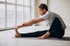 A man in workout clothes stretching his leg on a yoga mat.