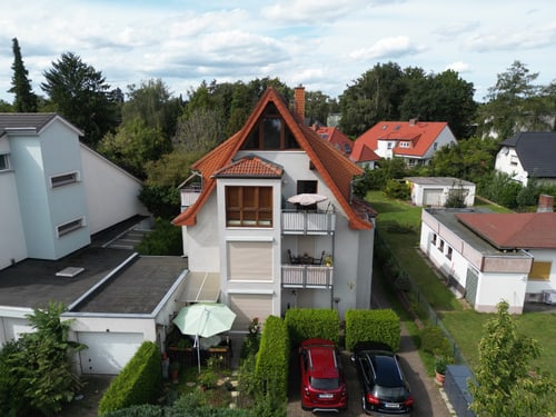 Dachansicht eines weißen Hauses mit rotem Dach, zwei Balkonen, kleinem Garten und zwei Autos.