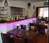 Bar mit lila beleuchteter Theke, Hockern und Tischen mit Schildern "1458 Angeln & Drinken".
