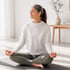 Woman sits cross-legged on a yoga mat, meditating in a sunlit room.