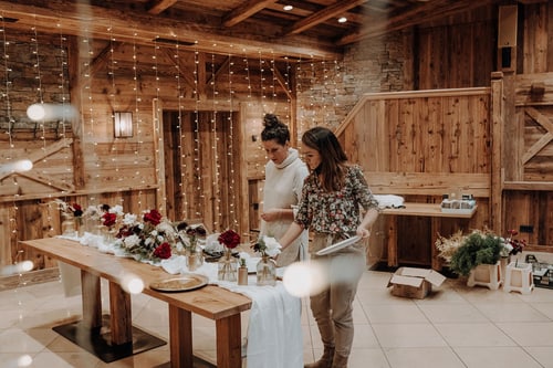 Zwei Personen dekorieren eine lange Tafel in der Almhütte