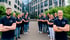 Ein Team von 16 Mitarbeitern in dunklen Poloshirts vor einem modernen Bürogebäude.