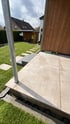 Moderne Terrasse mit hellen Steinplatten, Holzfassade und Blick auf eine Rasenfläche mit Trittsteinen im Garten.