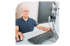 Mann mit Brille sitzt vor einem Computer, hält eine Maus und schaut auf den Bildschirm.