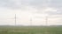 Drei Windräder in einer flachen Feldlandschaft im Dunst