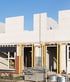 Concrete block house under construction with yellow support beams, scaffolding materials, and a blue sky.