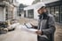 Bauarbeiter mit Schutzhelm und Jacke studiert Baupläne und Tablet auf einer Baustelle.