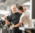 Ein älterer Mann trainiert mit einer Stange unter Anleitung eines Personal Trainers im Fitnessstudio.